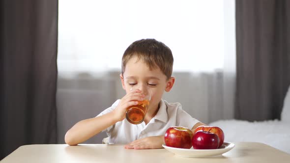 A Little Boy Sits at a Table and Drinks Fruit Juice. Happy Child Laughs. Concept of Healthy Food