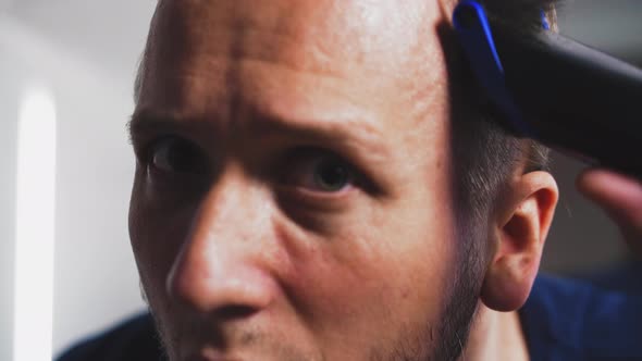 Nervous Man Shaves Head Using Trimmer in Brightly Lit Room