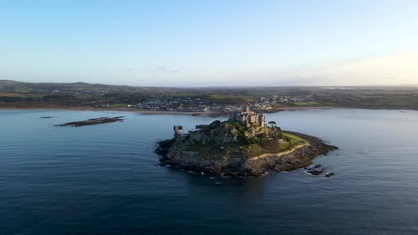 Aerial drone orbiting around St Michaels Mount during high tide and Marazion village in background,