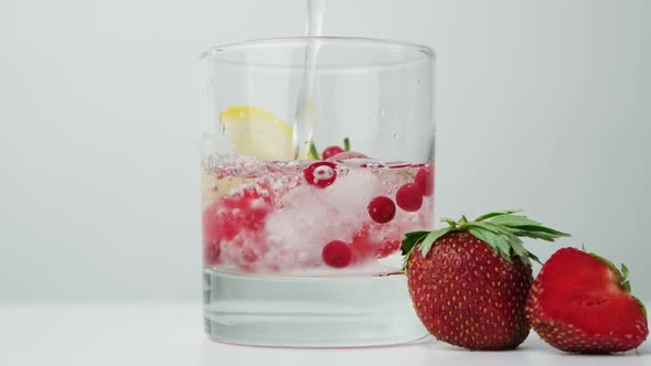 The Process of Pouring Water Into a Summer Cocktail with Strawberries Berries Lemon and Ice