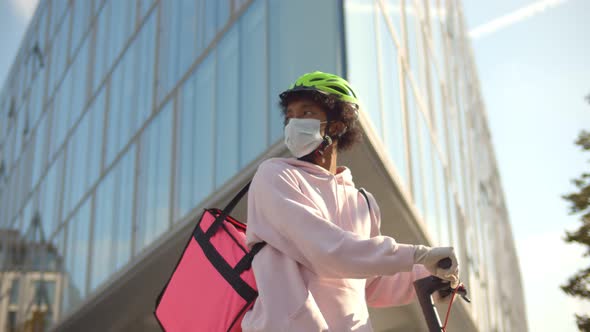 Young African Delivery Man in Helmet Wearing Mask Riding Electric Scooter, Delivering Food