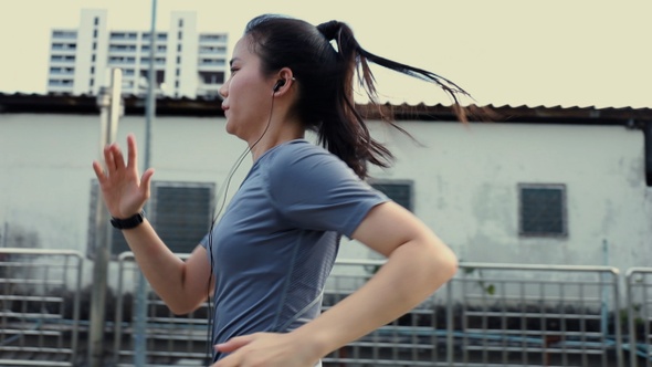 Beautiful Asian woman athlete wearing earphones listening to music running in the city.