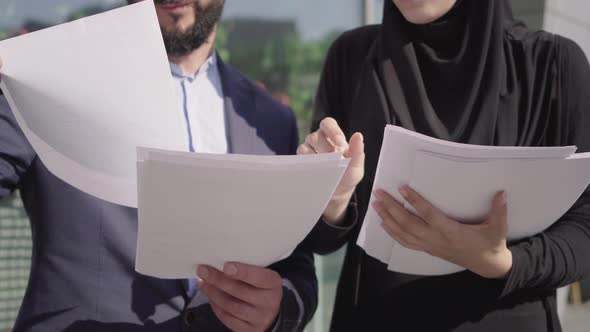 Confident Unrecognizable Middle Eastern Man and Woman in Hijab Passing Documents Outdoors on Sunny