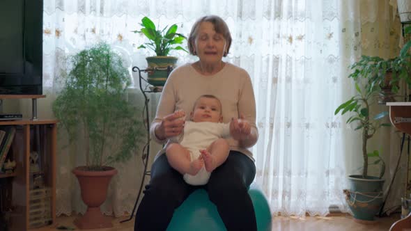 A Grandmother with Her Newborn Grandson on Her Lap Bouncing on a Yoga Ball Both Having a Fun Bonding