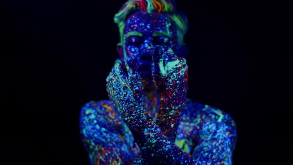 Dancing Man in Glowing Paint Under a Psychedelic Effect Examines His Hands and Looks at the Camera
