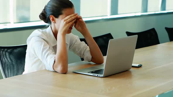 Executive crying while working on laptop in conference room