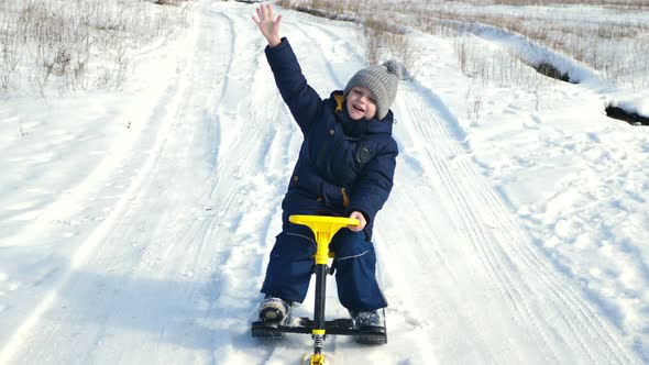 Little Boy Rides a Sled a Snowmobile in a Snowy Forest