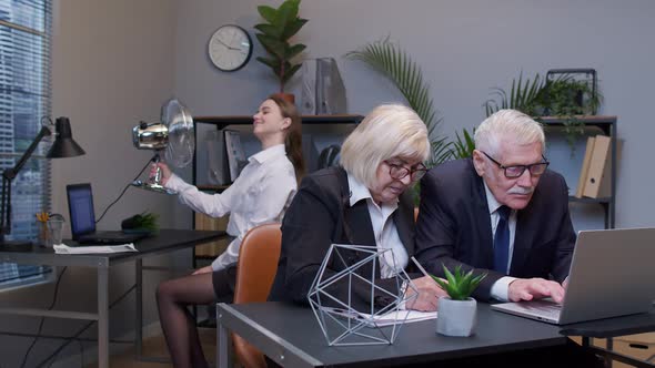 Elderly Man Boss with Woman Colleague Working in Office Secretary Relaxing with Electric Fan