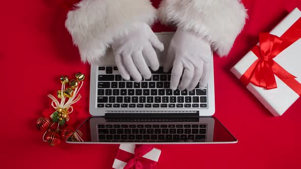 Top View Santa Hands in White Gloves Typing on the Keyboard By Red New Year Decorated Table
