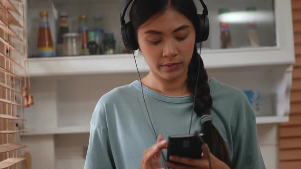 Young Asian woman using a smartphone inside the kitchen at home.