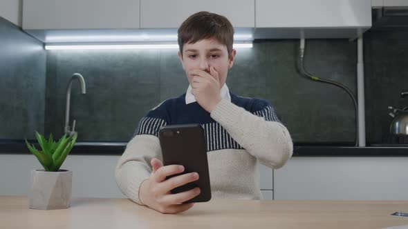 Afraid and Shocked Boy Look at Smartphone Screen Cover Mouth with Hand at Home Kitchen