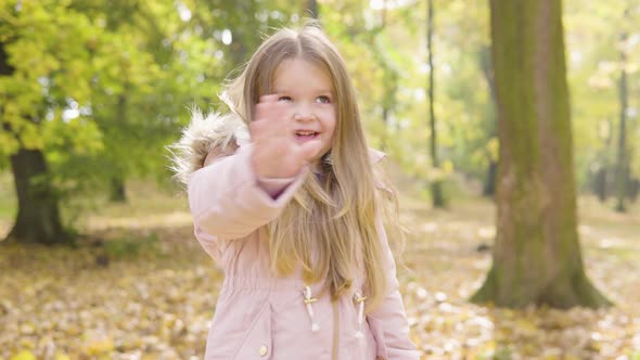 Cute Little Caucasian Girl Waves at the Camera with a Smile in a Park
