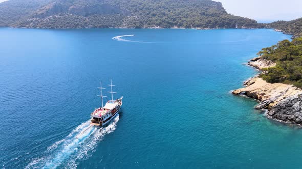 Drone fly over a bay in the Mediterranean over a yacht sailing between islands covered in green tree