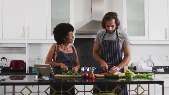 Mixed race couple wearing aprons chopping vegetables together in the kitchen at home