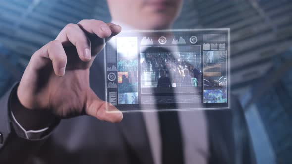 A Man Against a Background of Skyscrapers is Watching a Video on a Glass Tablet