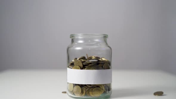 Coins in a Jar with Blank Label. Money Falling from the Sky Above in Slow Motion