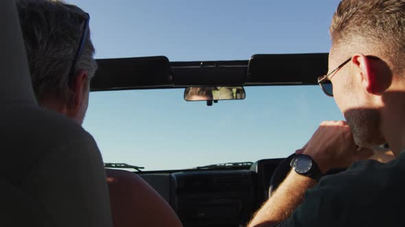 Happy caucasian gay male couple driving car and talking on sunny day at the beach