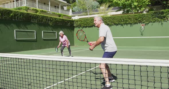Happy caucasian senior couple playing as a doubles team at outdoor tennis court after playing a game