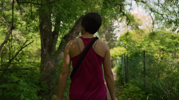 Woman wearing pink tanktop walking through a forest trail next to a fence on a sunny summer day. Slo