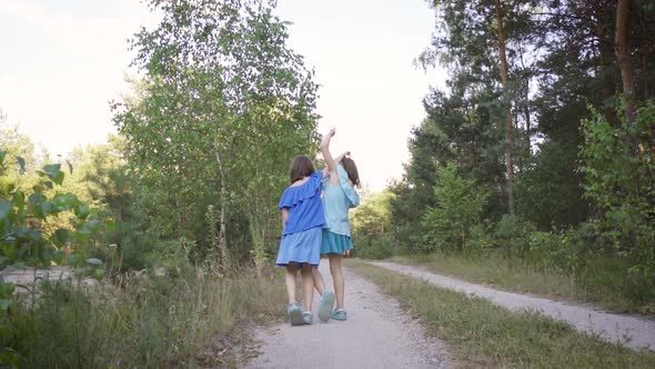 Two Cute Girls Are Walking Along the Forest Road and Talking
