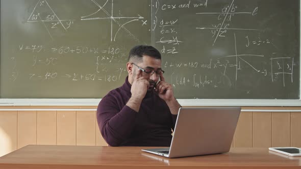 Tired Male Professor Massaging his Temples during Work on Laptop