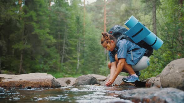 Woman Traveler Drinks Clean Water From River in Summer Forest While Hiking