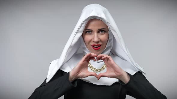 Slim Beautiful Woman in Nun Costume Showing Heart Gesture with Hands Looking at Camera Smiling