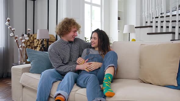 Young Pregnant Woman Relaxing on the Couch Together with Her Lucky Curly Husband
