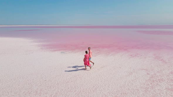 Aerial Epic Drone Image of Lovely Romantic Couple Walking Along Bright Colorful Pink Water of