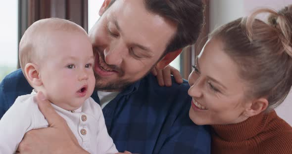 Young Happy Parents and Their Adorable Baby Next to the Window Bearded Father Holds His Baby and