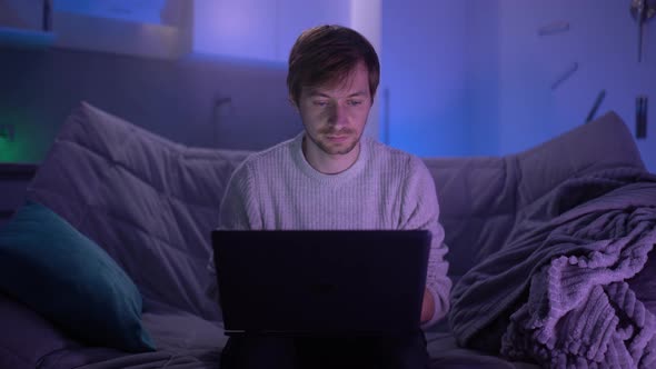 A Young Guy Sits on the Couch at Home and Communicates on Social Networks