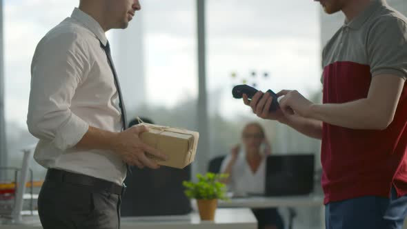 Side View of Employee Receiving Parcel in Office Paying with Credit Card for Delivery