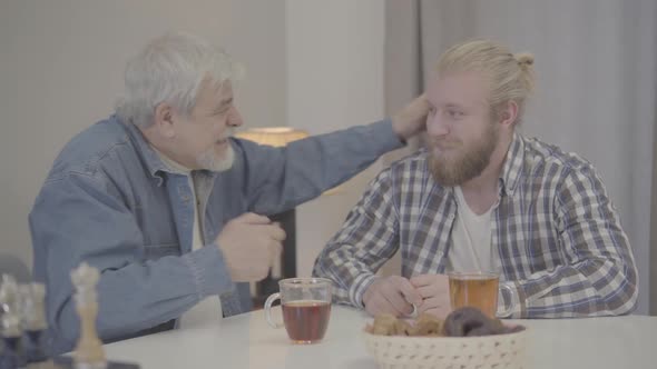 Young Caucasian Man Talking To Senior Father As Retiree Taking His Ear and Waving Finger. Joyful