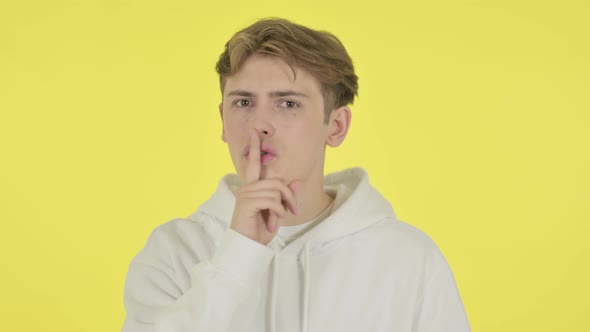 Young Man with Finger on Lips Silence Yellow Screen