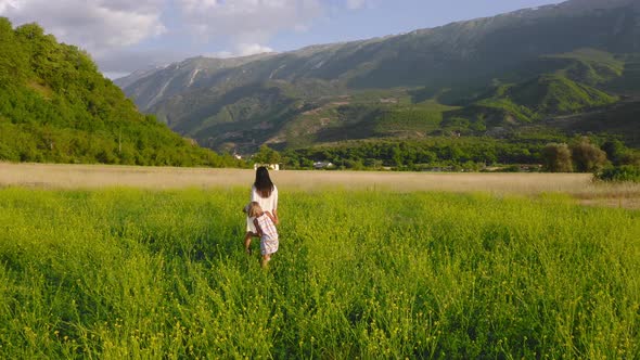 Young dark-haired mother with blonde child walking peacefully and free in green field in European va