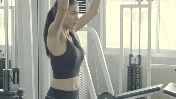 Beautiful young asian woman doing pull down exercise with hand on machine in the gym.