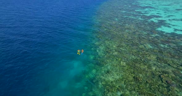 Aerial drone view of a man and woman couple snorkeling over a coral reef of a tropical island