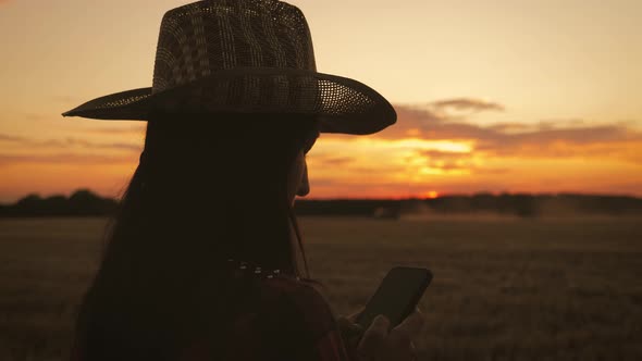 Silhouette Woman Farmer in Hat Standing with Wheat of Harvest Against the Background of a Sunset