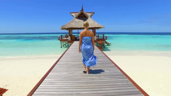 A woman walking on a dock pier over a tropical island beach.