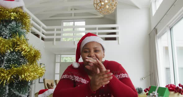 Happy african american plus size woman wearing santa claus hat, making video call at christmas