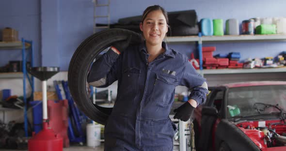 Portrait of female mechanic holding a tire and smiling at a car service station