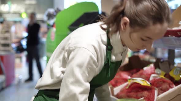 A Young Saleswoman in an Apron is Examining the Cabbage for Quality