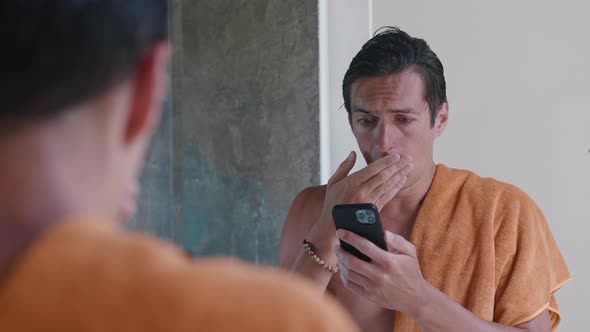 Worried Man Looking at Smartphone and Shocked By Bad News Covering His Mouth with His Hand in Horror
