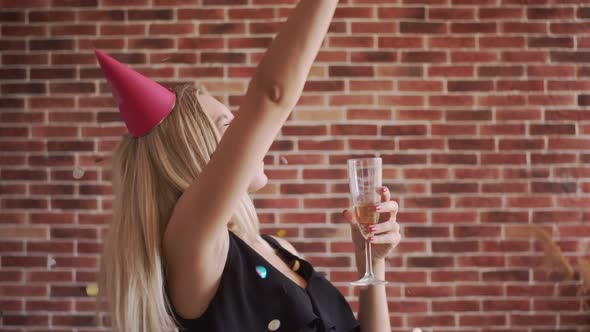 A Happy Girl at a Party with a Glass of Champagne Is Having Fun, Confetti Falls on Top of Her