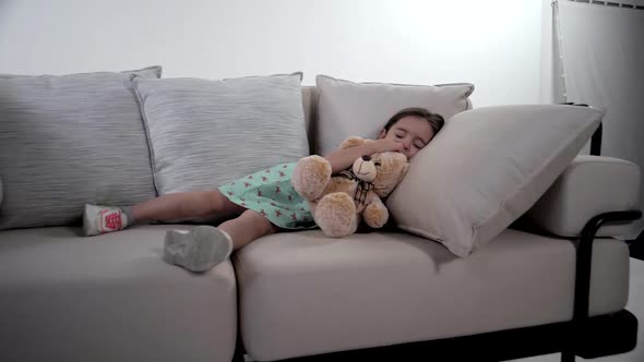 Baby girl falling asleep on a comfortable couch with a teddy bear in her hands