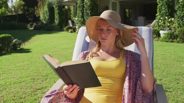 Caucasian woman reading a book while sunbathing on a deck chair in the garden