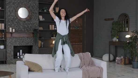 Young Funny Happy Carefree Cheerful Woman Housewife Actively Moves Dynamically Dances on Sofa in