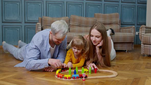 Family of Mother Father with Daughter Child Girl Riding Toy Train on Wooden Railway at Home Room