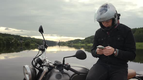 Motorbike Driver Messaging and Looking at His Phone Sitting at the Sunset