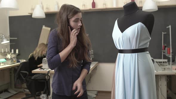 Busy Caucasian Beautiful Female in Dark Blue Shirt Talking on Mobile Phone in Sewing Classroom